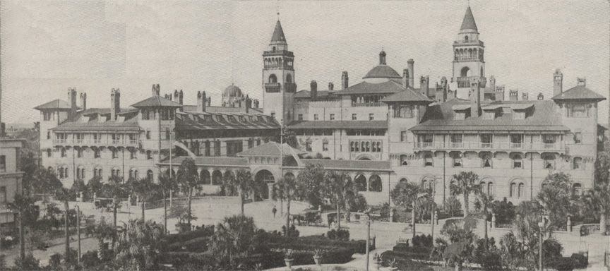 A black and white panoramic photograph of the Ponce de Leon Hotel in St. Augustine, Florida, circa 1915. The lush courtyard of the Alcazar Hotel can be seen in the foreground, with Ponce's extensive spires visible in the background.