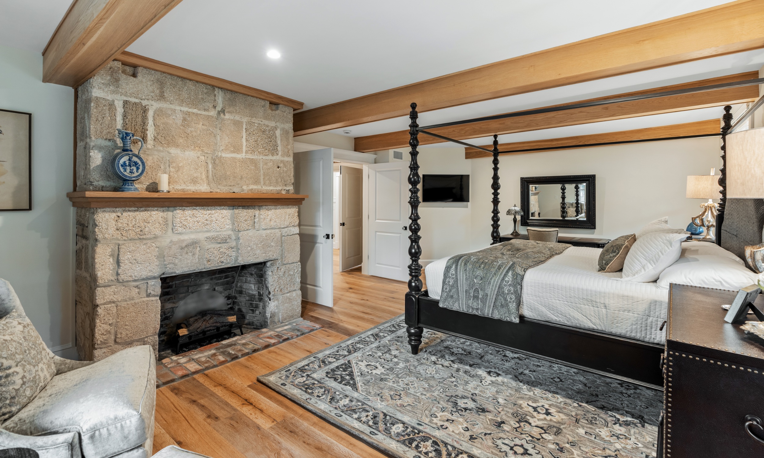 This large bedroom has a fireplace, large wood beams, and four-poster bed