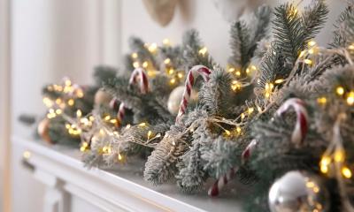 Greenery on a fireplace mantle decorated with gold and silver ornaments and lights