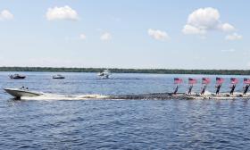 A boat towing a line of water-skiers, all holding American flags, on a lake in Florida