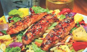 A salmon salad with three generous slabs of blackend salmon on a pile of greens, vegetables, and fruits