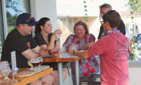 A beer tour group enjoy small glasses of different beers, outside on a deck in the sun