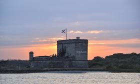 A sunset view of Fort Matanzas with the crew standing on the deck and the flag flying