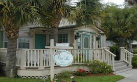 The Cozy Inn Office viewed from San Marco Avenue. Its porch and entryway are painted in inviting pastels, with palm trees and roses in the yard.