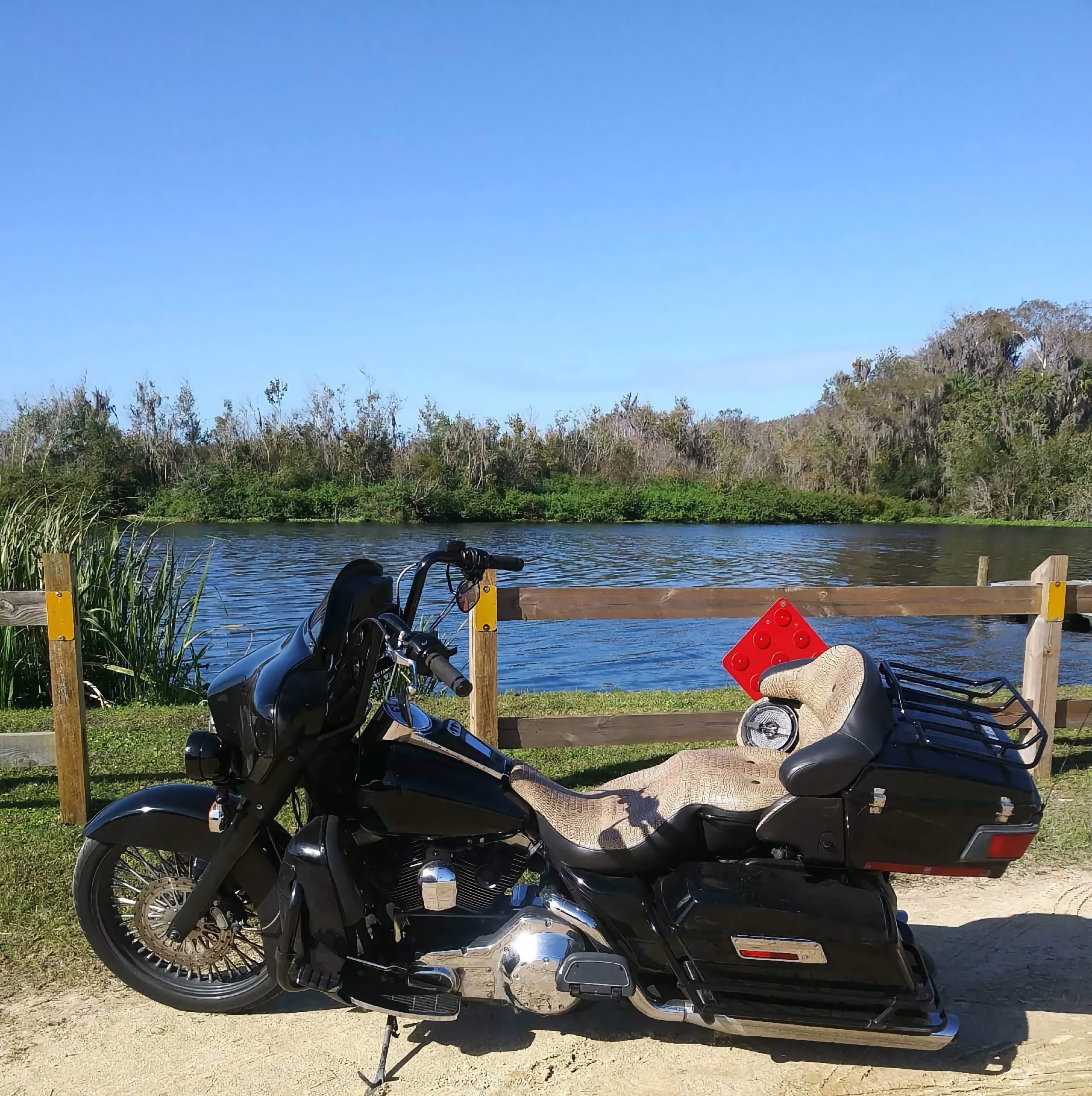 Black motorcycle siting in front of a wooden fence with a lake behind the fense