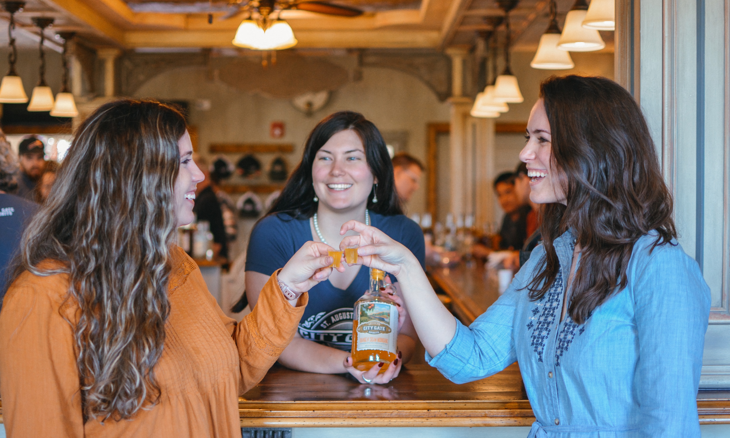 Two women toasting each other, in front of the City Gate Springs tasting bar and female Tasting Guide