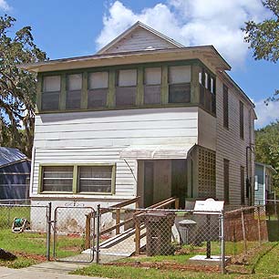 A photograph of a three-story home in St. Augustine, Florida. It is white wood with green window frames and doors. Facing the street on the ground floor is a ramp for the resident's accessibility. The ACCORD Freedom Trail Plaque can be seen behind the chain link fence.