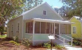 A photograph of a house in St. Augustine, Florida. It is a two-story home with sea foam green paneling on the outside and white accents on the porch, windowsills, etc. There is a small plaque in front of the house.