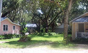 A photograph of an empty lot in St. Augustine, Florida on Gault Street in West King. Trees cast shadows on the sunny grass yard that used to be the Roberson home. In front of the steps is the ACCORD freedom trail plaque.