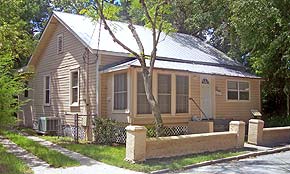 A photograph of a beige home in St. Augustine, Florida. The house is two stories with white accents on the window frames and doors. There is a tall and thin tree in the front yard.