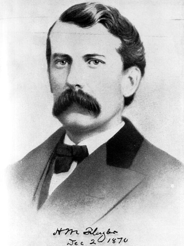 A black and white portrait of Henry M. Flagler in the 1870s — he had dark hair and a large dark mustache. He wears a suit and ties and looks directly at the 'camera.' Text at the bottom of the image reads: H.M. Flagler Dec 2 1870 in cursive handwriting.