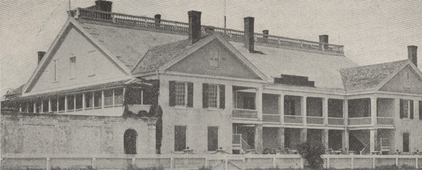 A black and white photograph of the St. Francis Barracks as they appeared in 1915. It is a large building with man windows and chimneys and a balcony on the second floor.