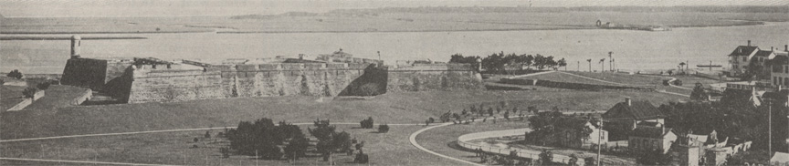 A black and white photograph of an aerial view of the Castillo de San Marcos, circa 1915. The fort lawn and its paths are visible, as well as the north end of downtown St. Augustine, Florida. The Matanzas Bay can be seen at the top edge of the image.