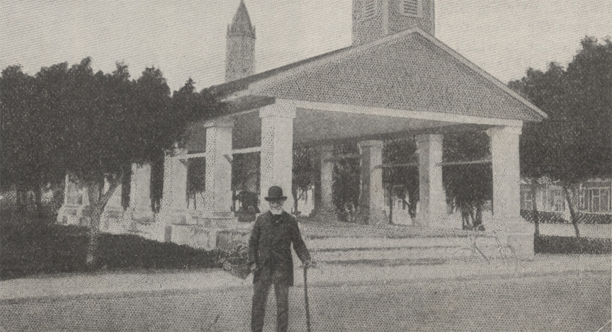 A black and white photograph of the Public Market in St. Augustine, Florida, circa 1915. It is an open air gazebo structure. An older man with a cane poses in front of the market.
