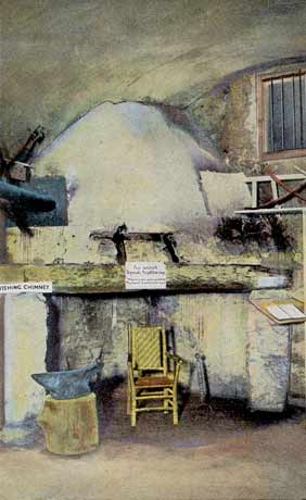 A color-tinted photograph of an interior room of the Castillo de San Marcos (then Fort Marion), circa 1920s, in St. Augustine, Florida. It shows a chair sitting in front of a fireplace with a flat mantle. The stone walls look to have some sort of plaster on them, appearing flatter and whiter than other images of coquina stone. 