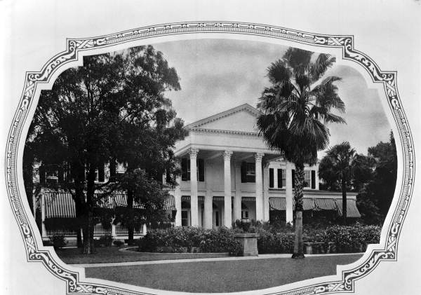 A black and white photograph of an estate in St. Augustine, Florida called Kirkside. It has white columns, a triangular roof, and is surrounded by palm trees and oak trees.