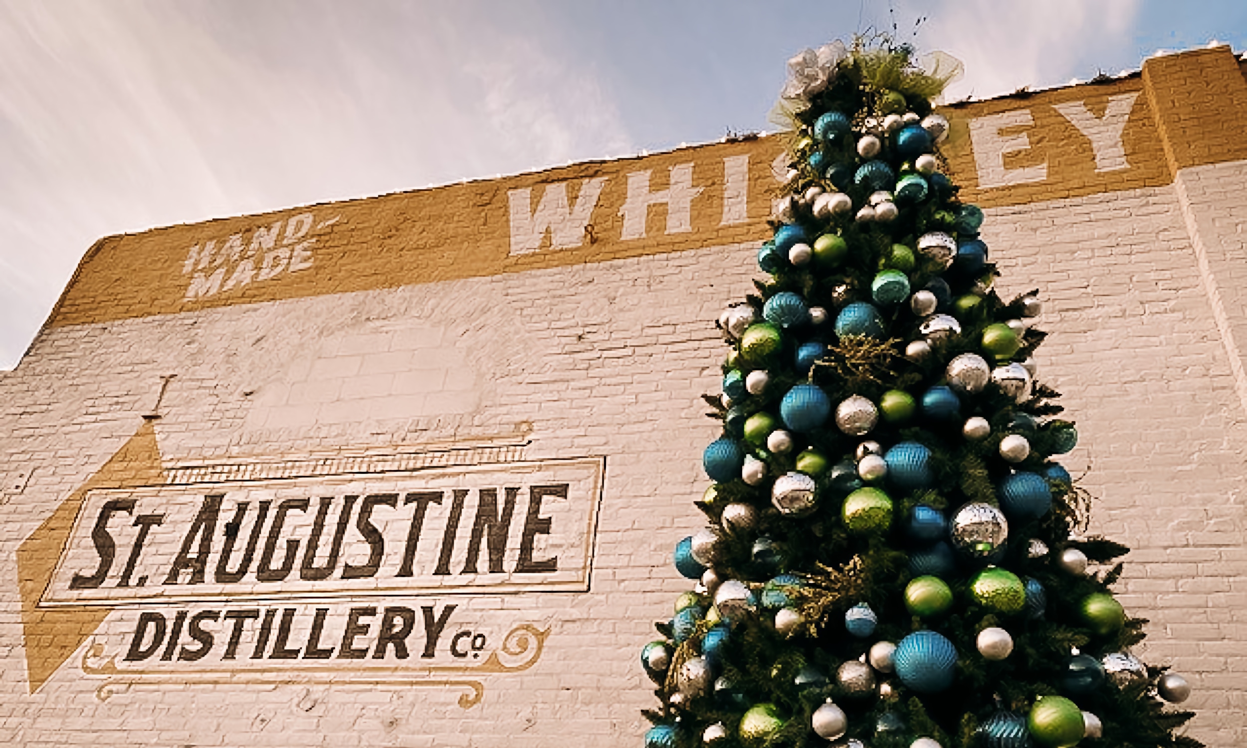 A tall Christmas tree with colorful globe ornaments, in front of the St. Augustine Distillery Building