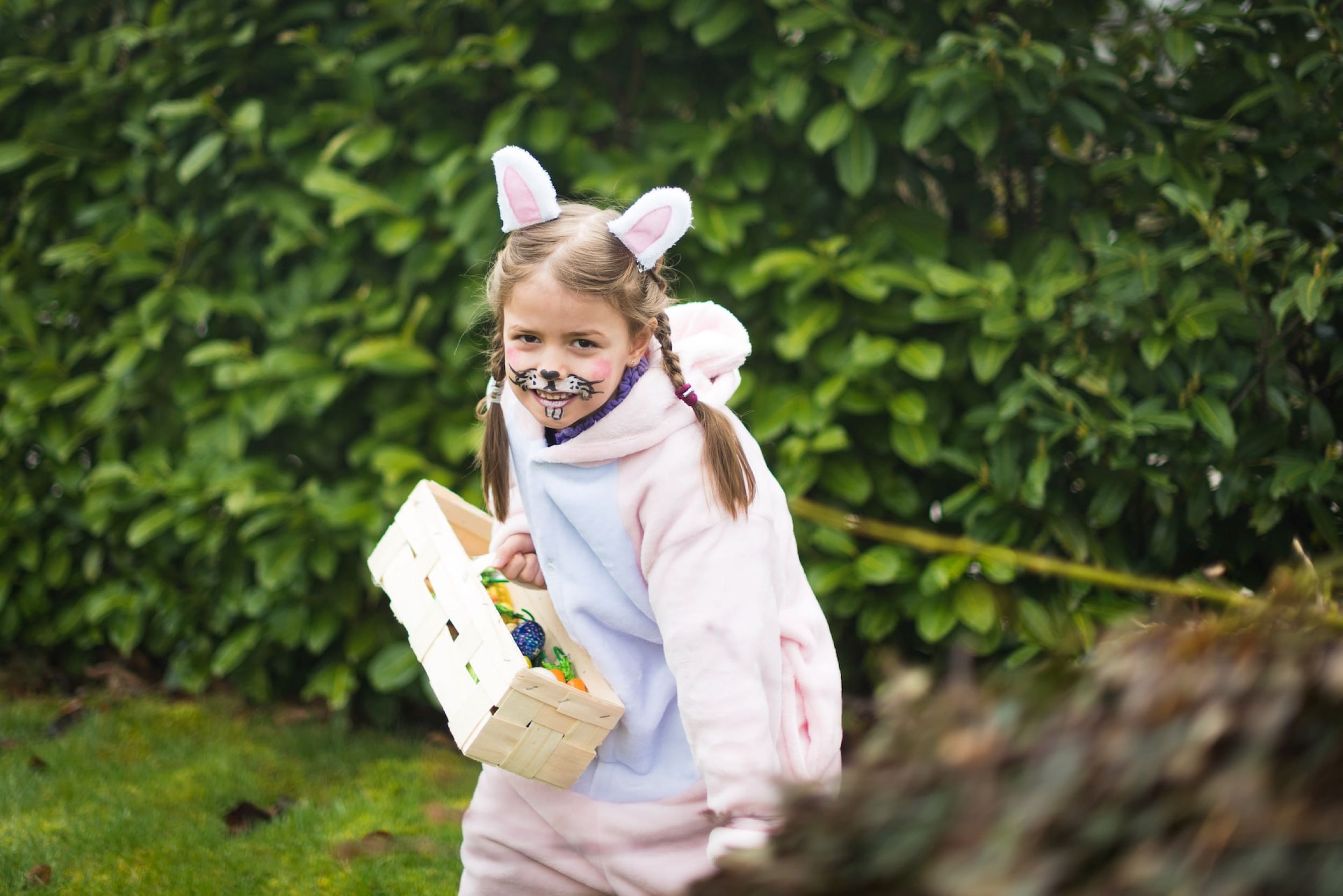 A girl dresses as the Easter bunny and holds a basket filled with colorful eggs.