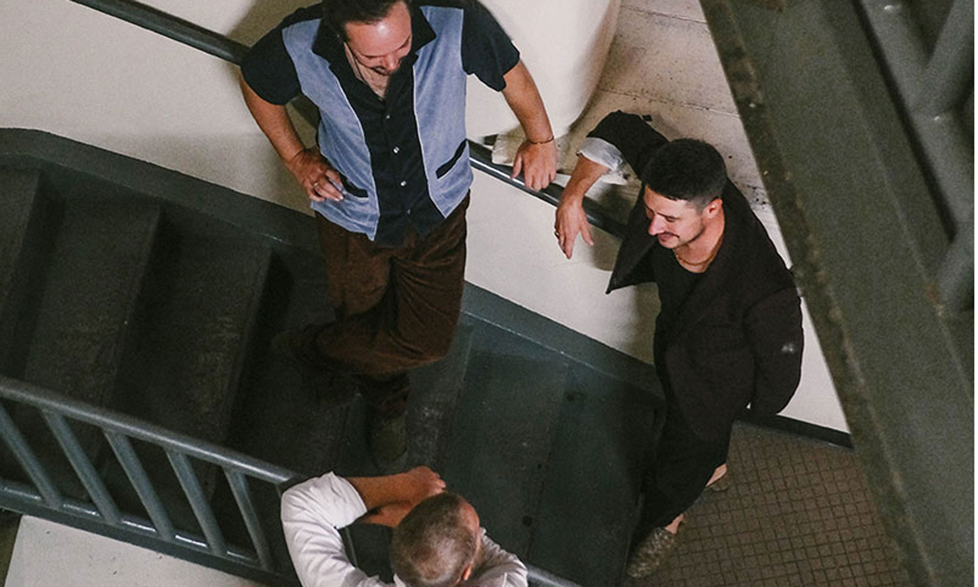 The three members of Mumford and Sons, as seen from above, chatting on a stairway