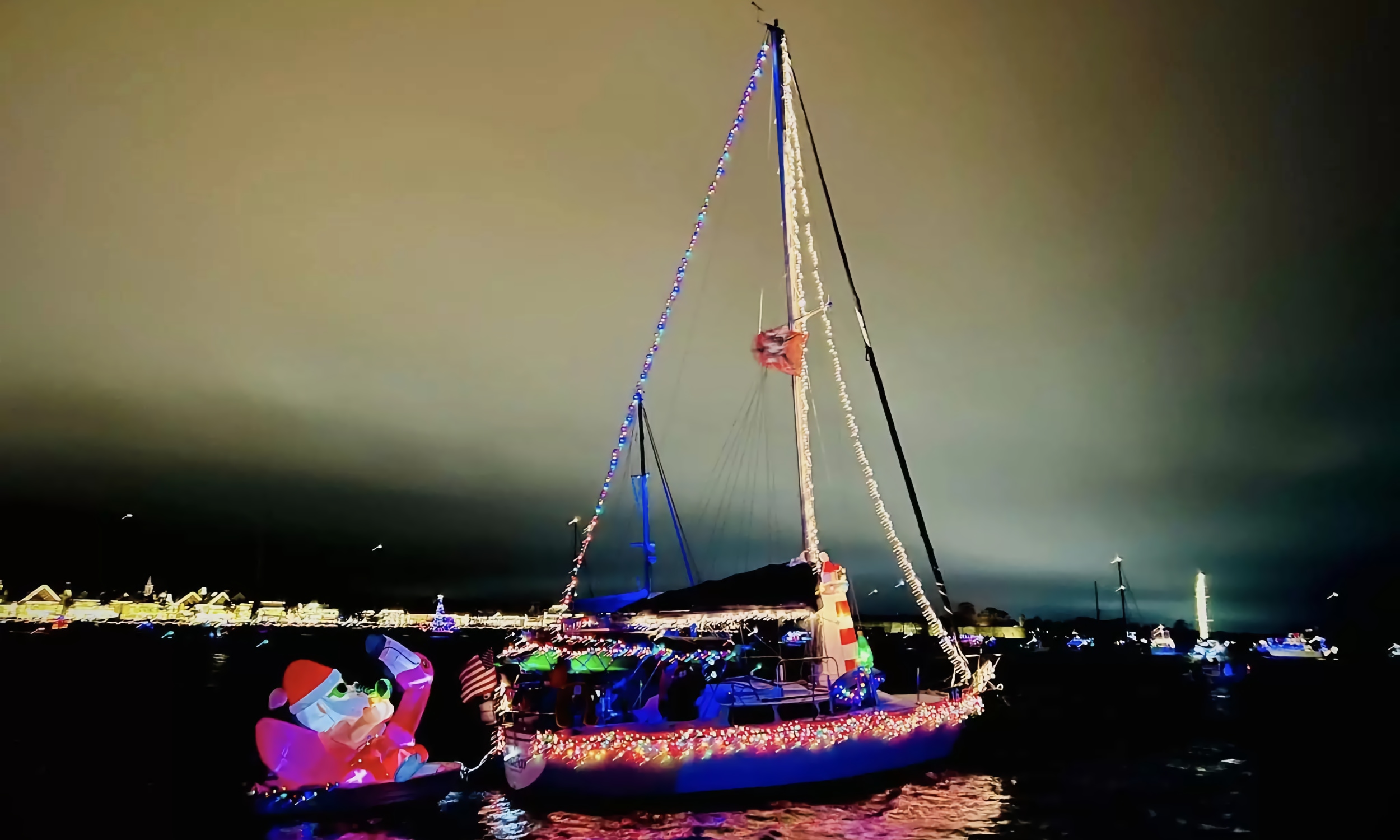 A sailobat towing Santa's Sleigh, all decorated in multi-colored lights against the St. Augustine shore for the Regatta of Lights