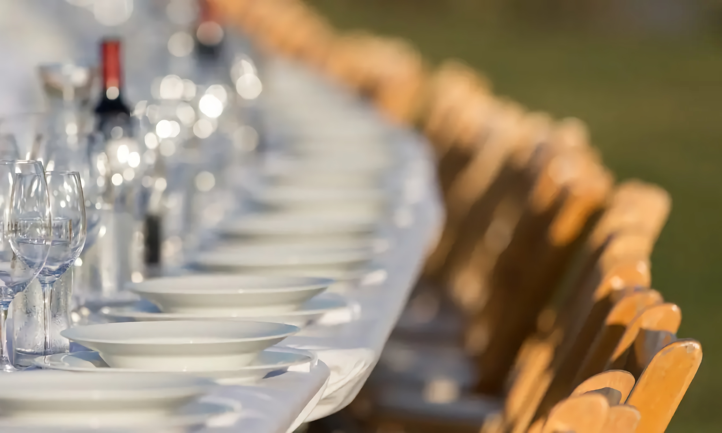 A banquet table, arranged outdoors with white plates, wine glasses, and wine