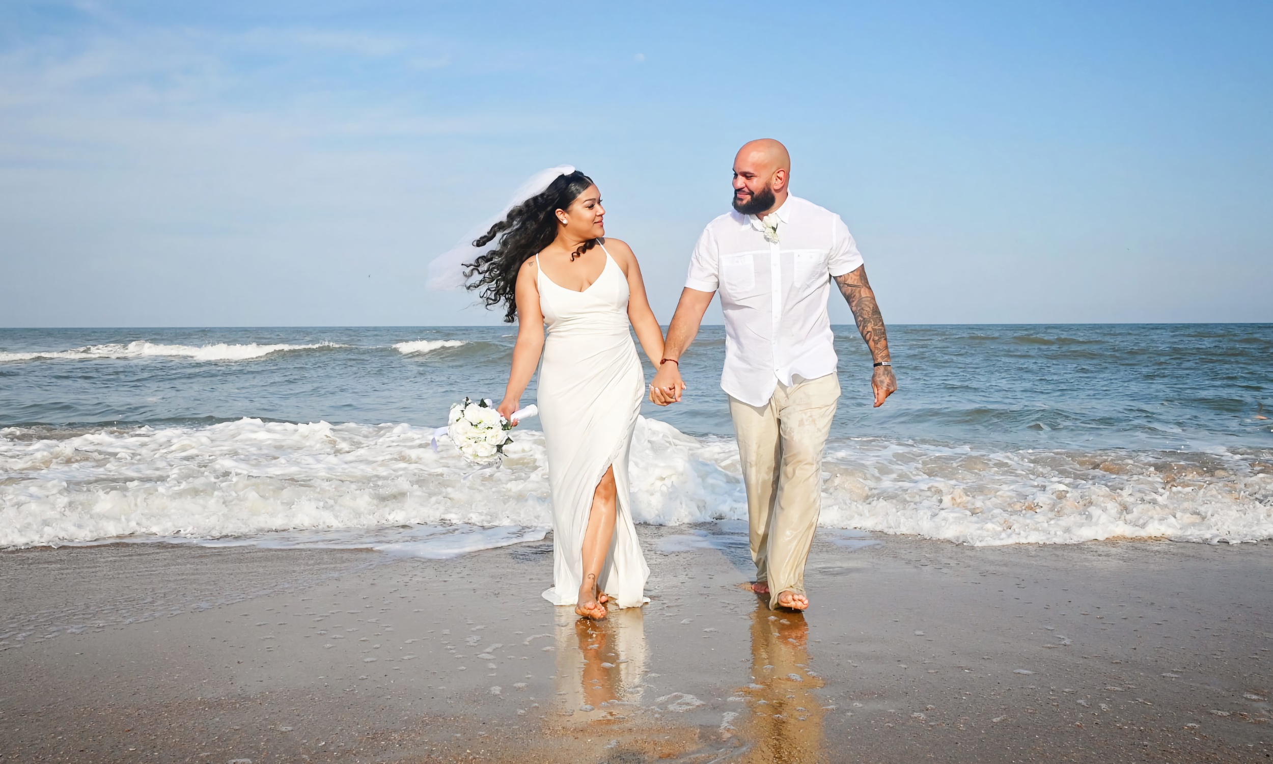 A bride and groom walking hand in hand at the beach
