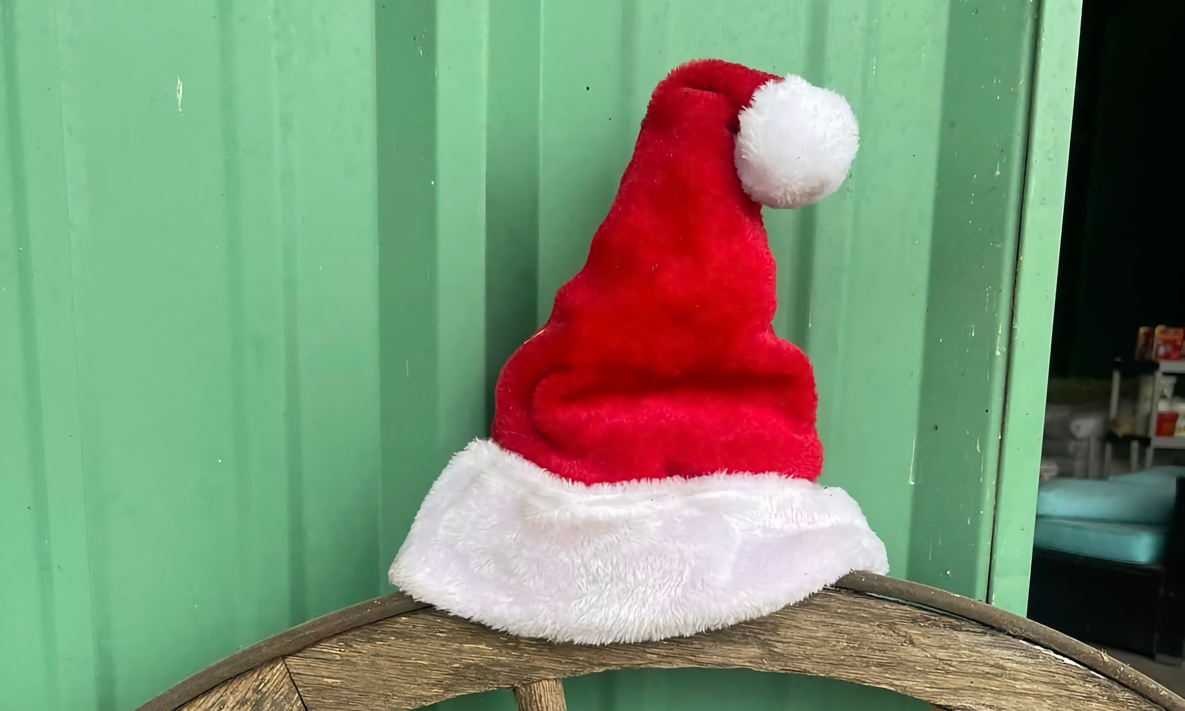A Santa hat atop a wagon wheel in front of a bright green barn 
