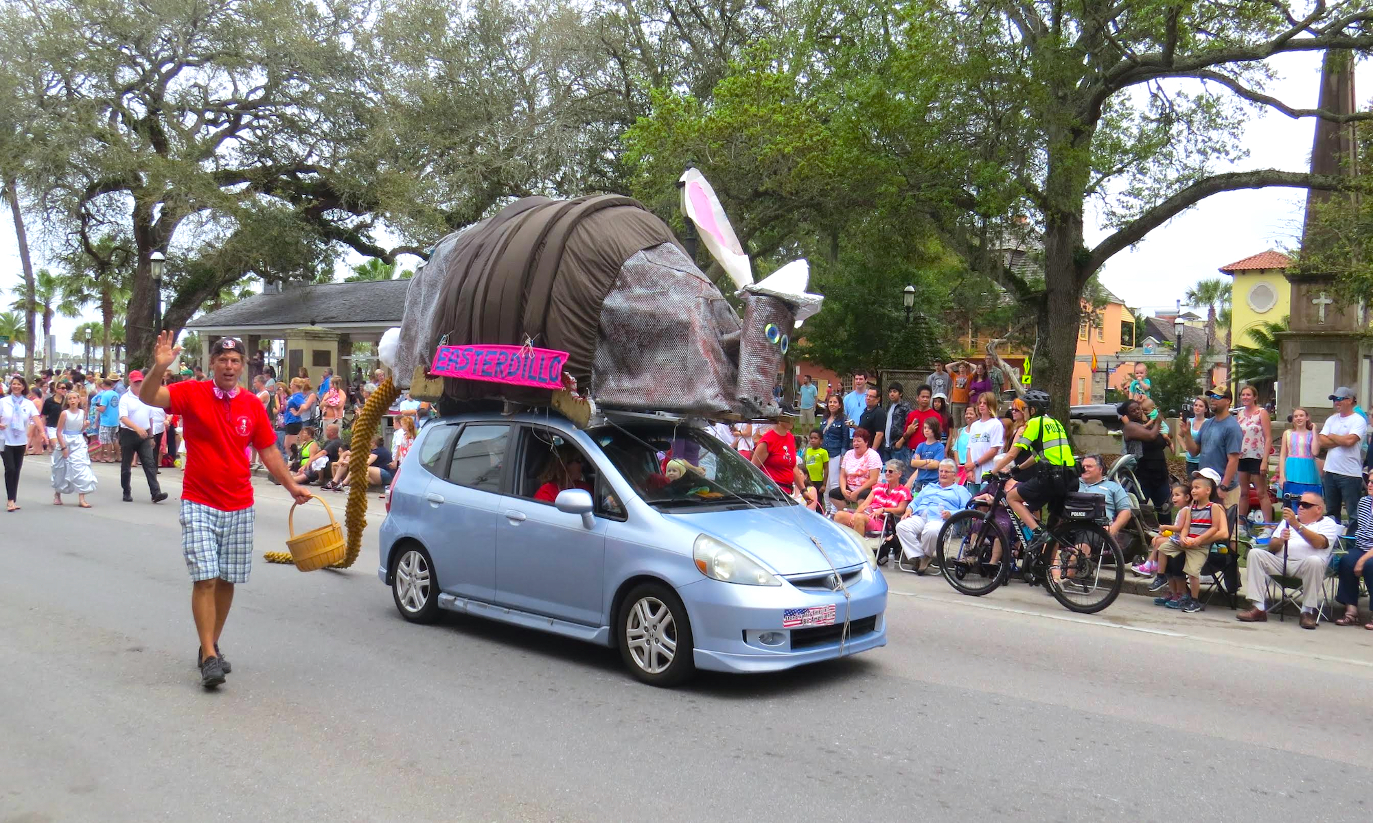 A car in the Easter Parade, with a handmade armadillo on top, and onlookers admiring it.