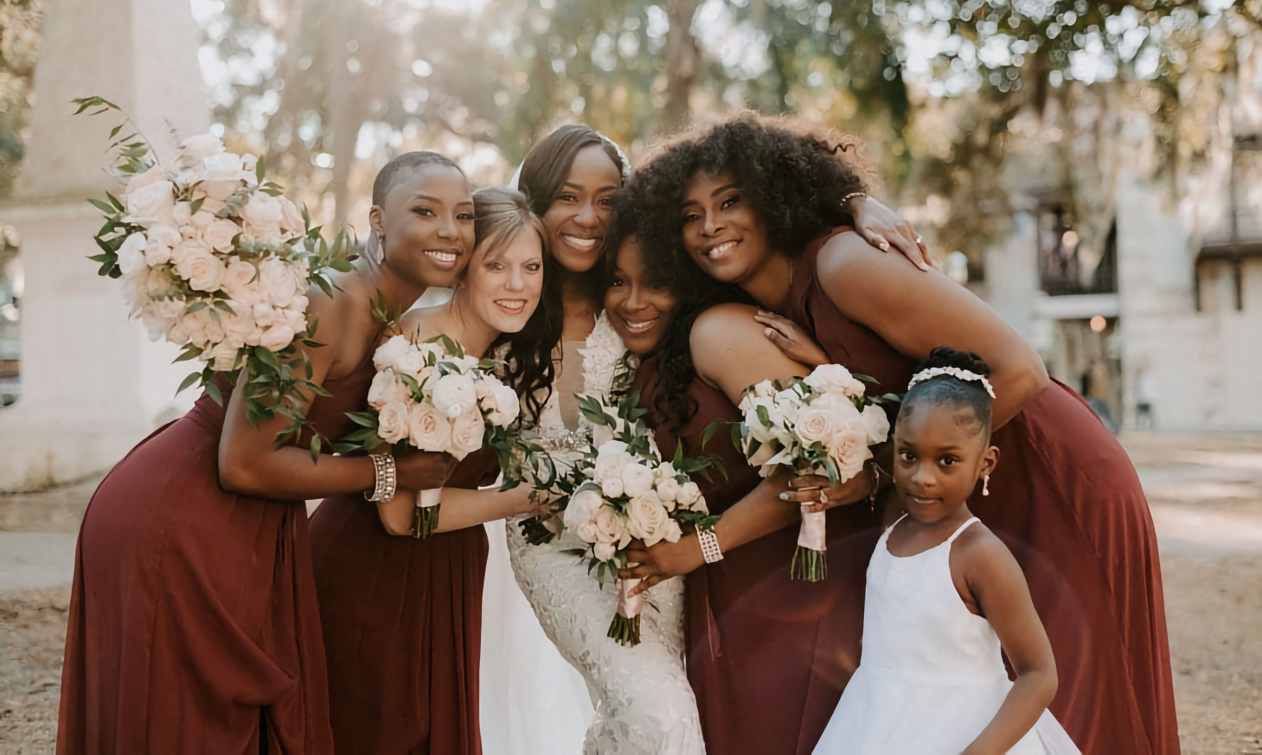 A bridesmaids party, five women and a young girl, embrace in the Plaza de la Constitución, bouquets in hand.