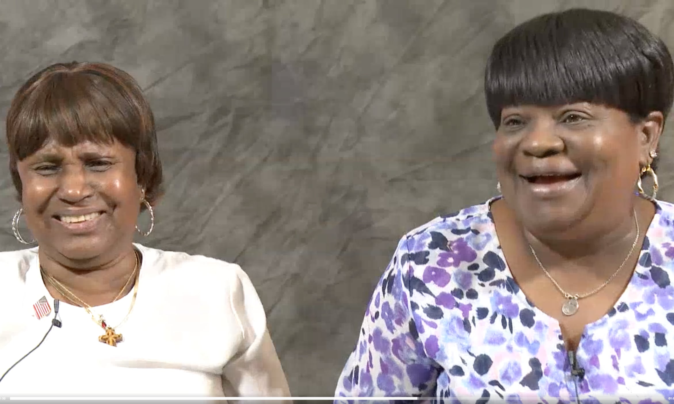 Shoulders up, Audrey Nell Hamilton and JoAnn Anderson Ulmer (older Black women) laugh in front of a grey backdrop.