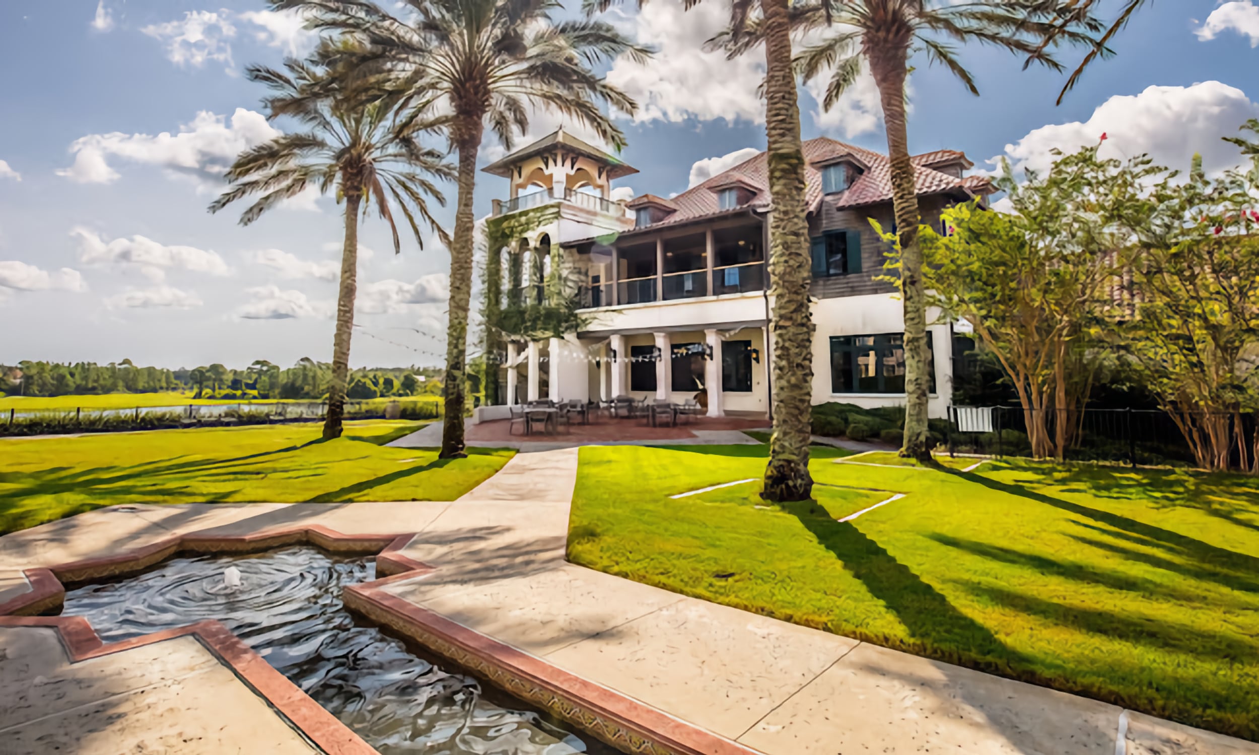 Palencia clubhouse with its Spanish-inspired architecture, flanked by palm trees and court pond, overlooking the golf course