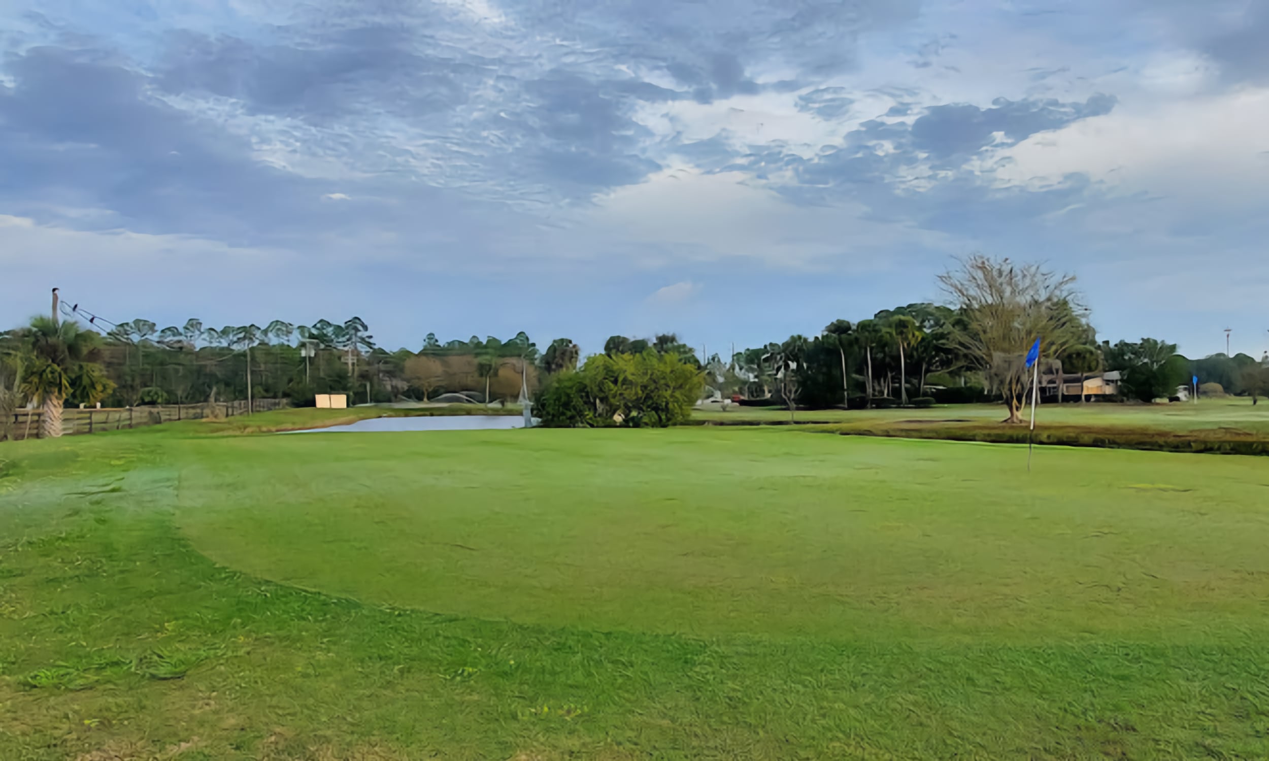 A ground view of Palm Valley Golf Club featuring a lush green, flagstick, and surrounding water hazards
