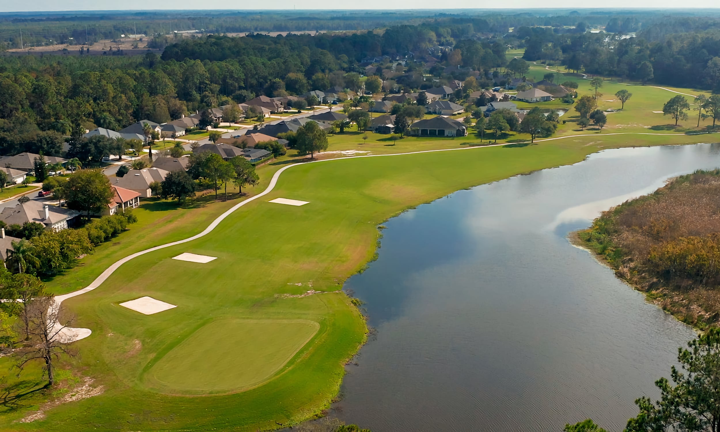 Aerial view of St. Johns Golf Club fairway, sand bunkers, and a large water hazard snaking through the landscape