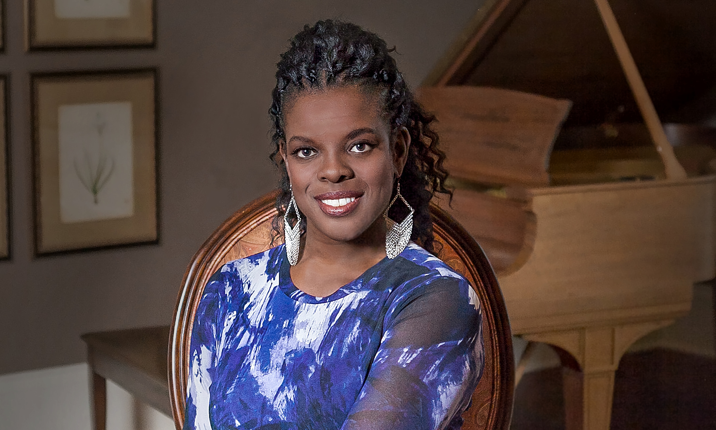 Soprano Ann Marie McPhail, wearing a white and blue dress and sitting with a light wood-toned piano behind her