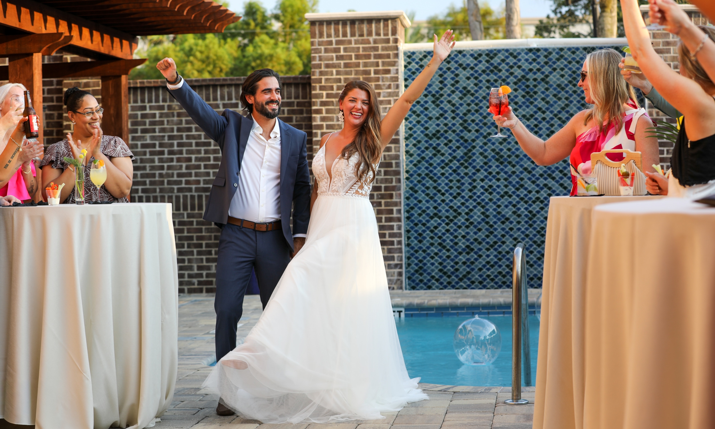 A bride and groom greet their guests on the pool patio