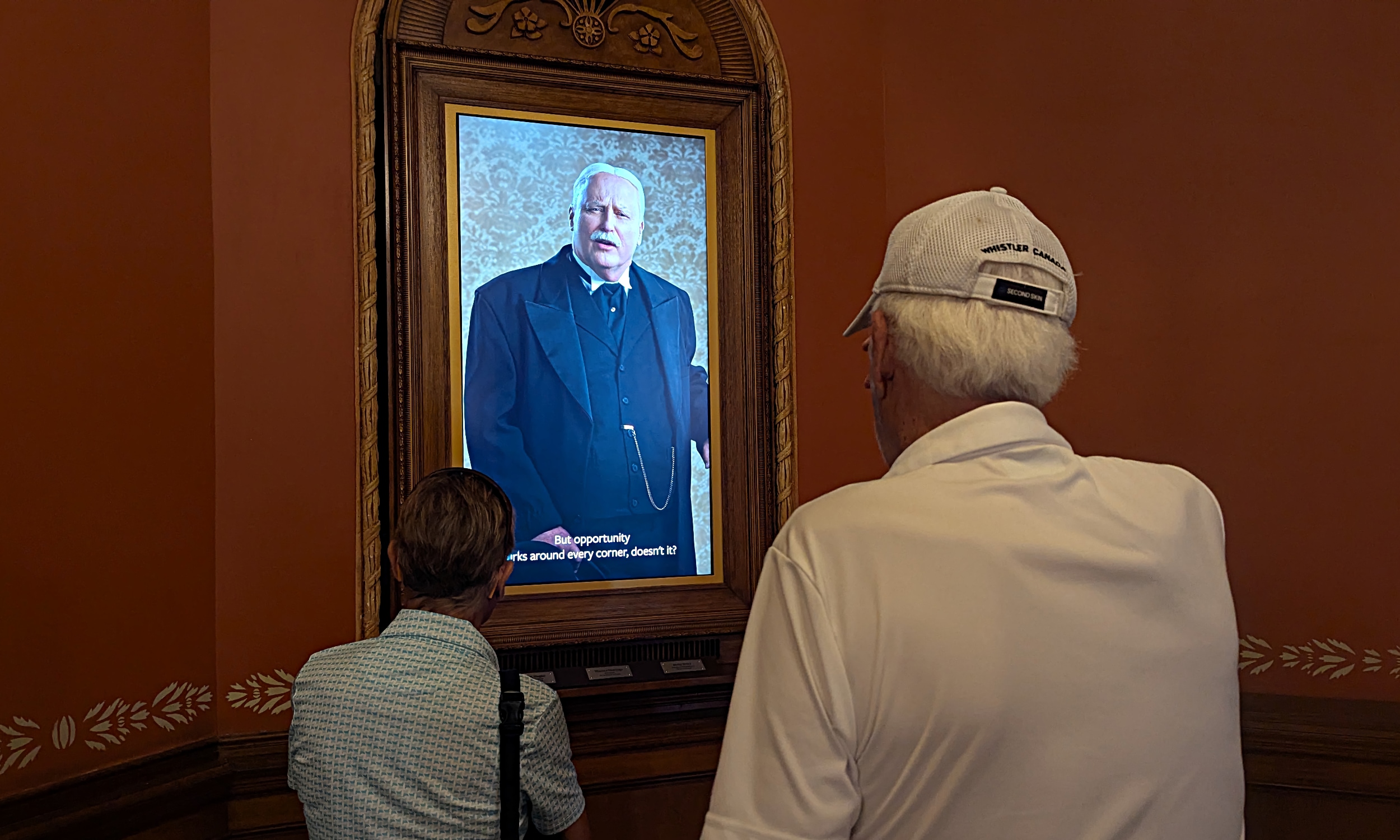 Two visitors listening to the video of an actor portraying Henry Flagler