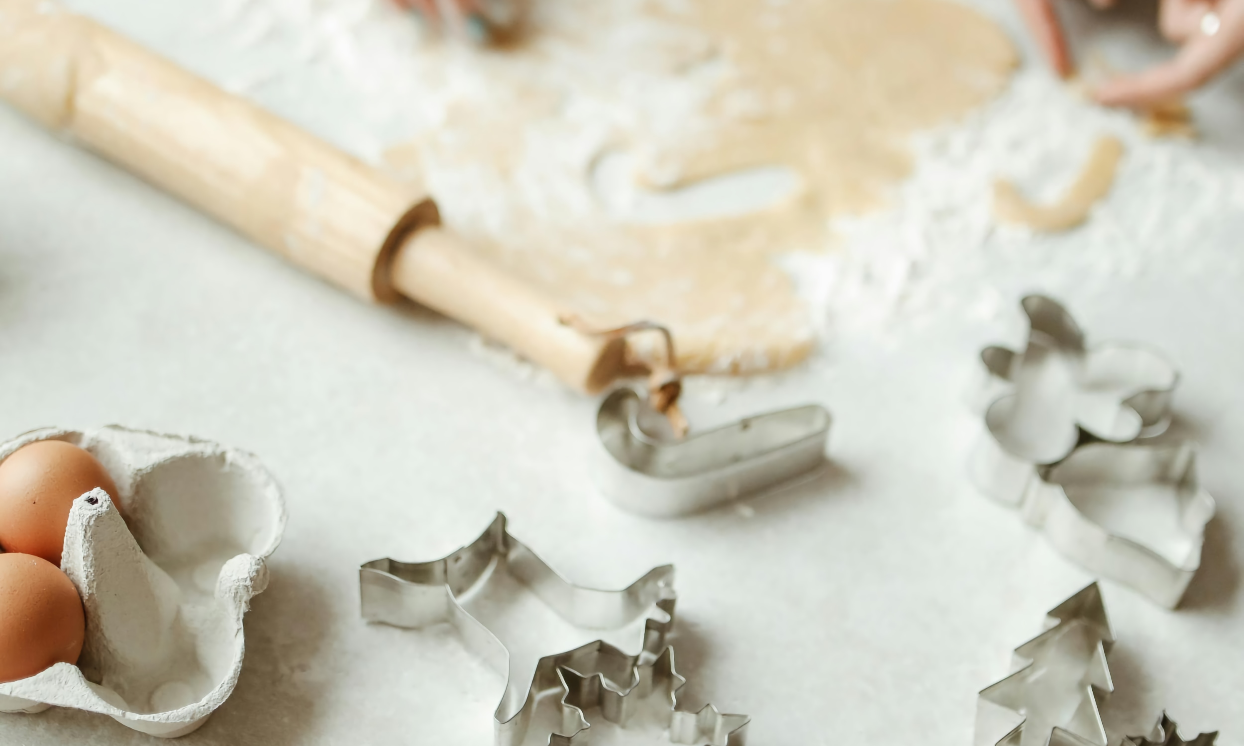 A kitchen counter, with holiday-shaped cookie cutters, dough, and a rolling pin