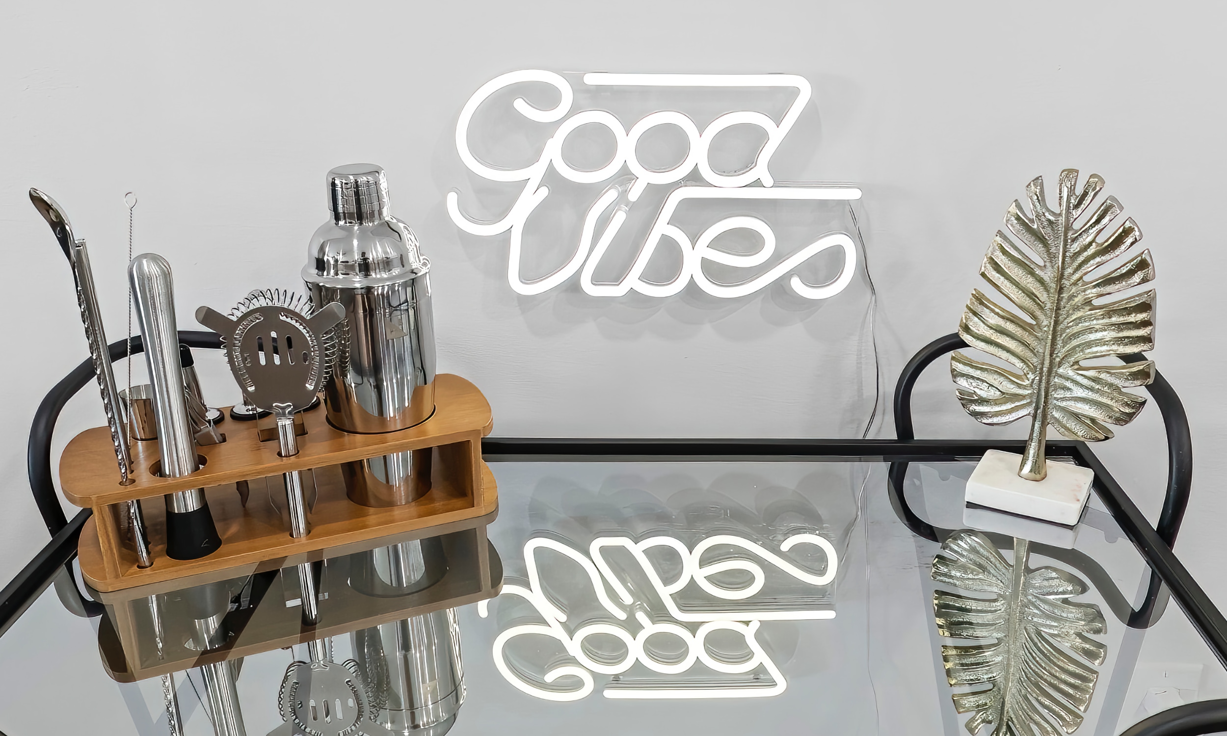 A drinks cart with mixing tools under a small neon sign spelling out "Good Vibes"