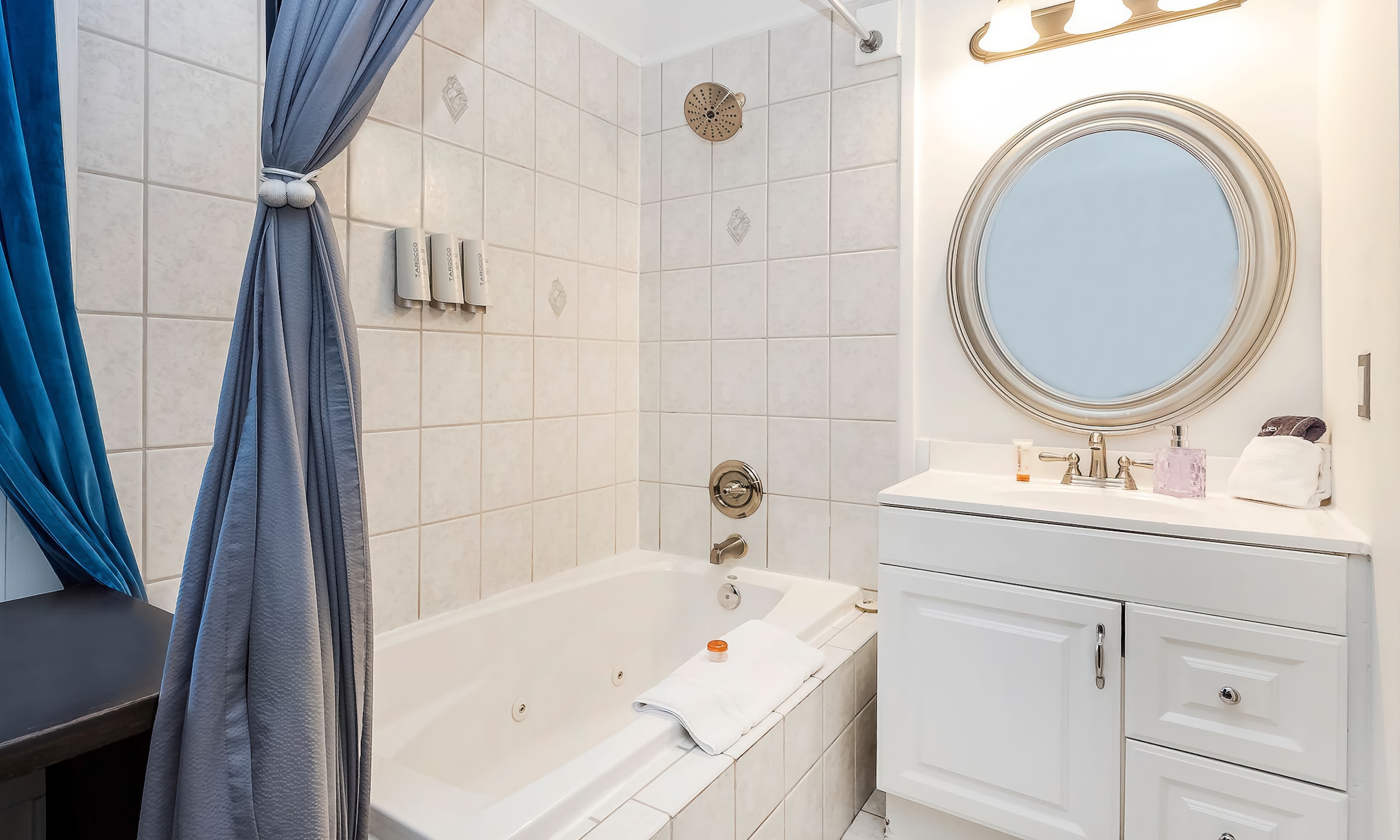 A white bathroom with gold fixtures, blue cuirtains, and a jetted tub