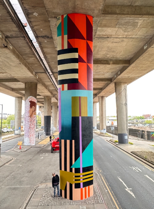 A man standing next to a massive column covered in a mural by Ansley Randall