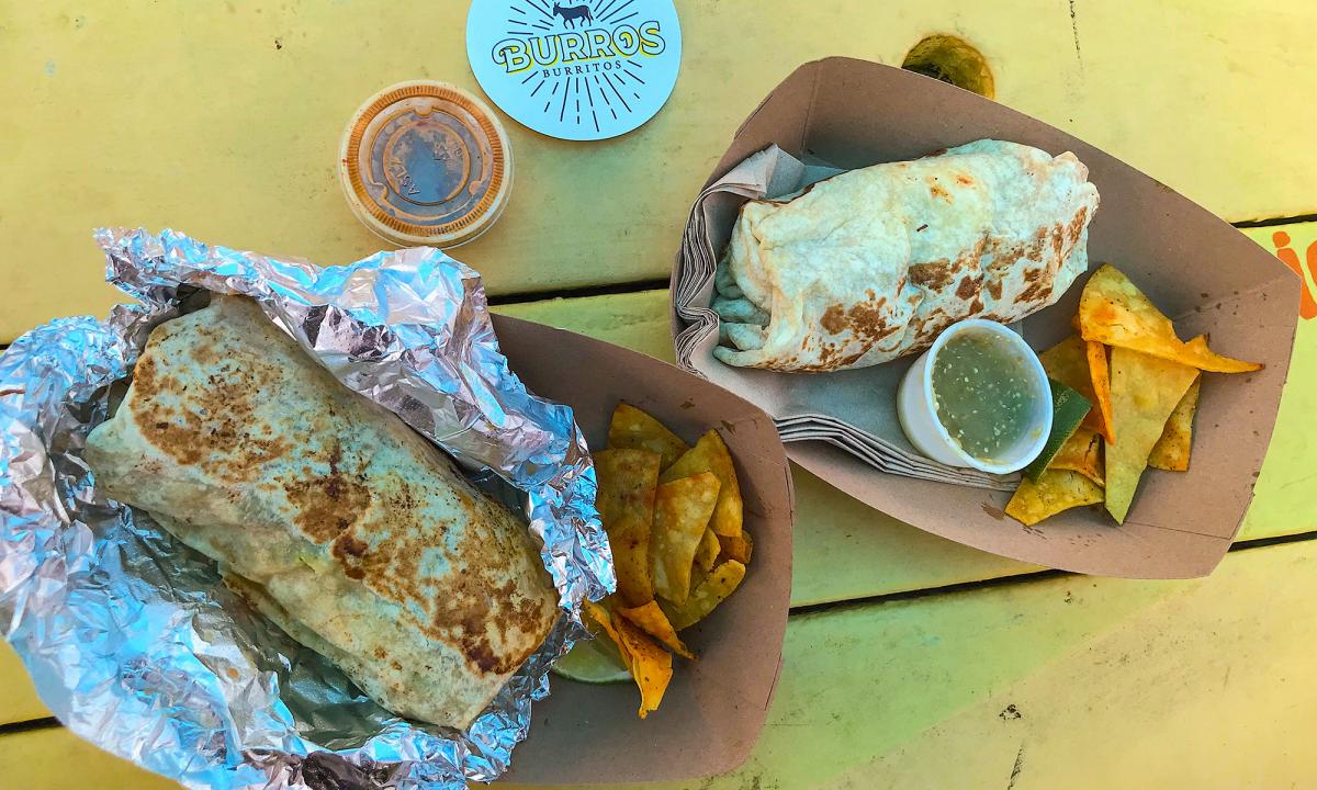 A table with two burritos and a logo sticker from Burros Burritos in St. Augustine, Florida.