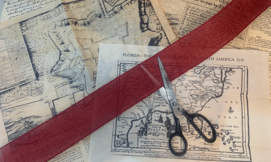 Old maps with red ribbon and scissors