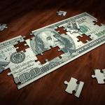 A partially completed puzzle of a one hundred-dollar-bill on a dark wood table