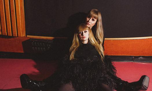 The two women who lead the band Lucius, wearing black and sitting on the floor 