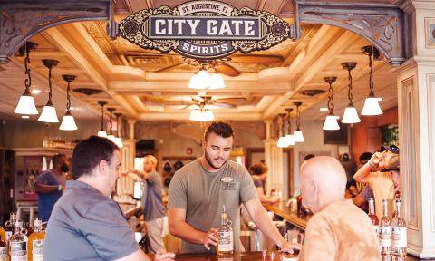 Two patrons and a server at City Gate Spirits, sitting and standing at the end of the tasting bar, with lights and detailed ceiling above them