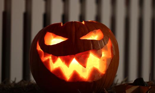 A brightly lit jack-o-lantern in front of a white picket fence