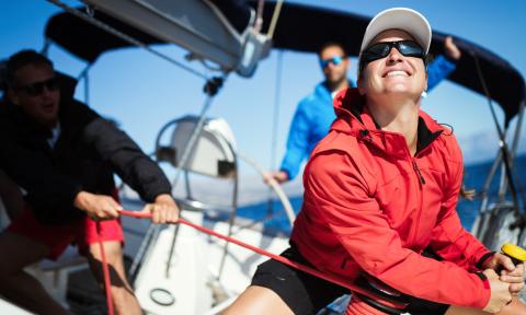 Three people sailing a sloop, a woman in the foreground at the winch