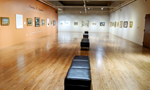 A long gallery with hardwood floors, black benches, and art on the walls