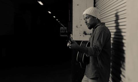 Mishka strums his guitar and concentrates on his music. 