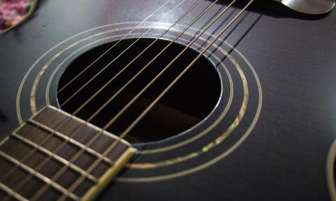 The front of a dark six-string guitar with gold-toned highlights